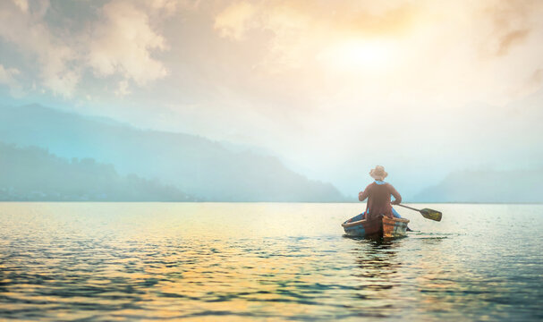 Back view of lonely fisherman in boat on morning lake
