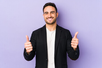 Young caucasian man isolated on purple background smiling and raising thumb up