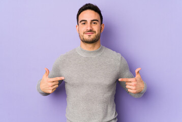 Young caucasian man isolated on purple background person pointing by hand to a shirt copy space, proud and confident