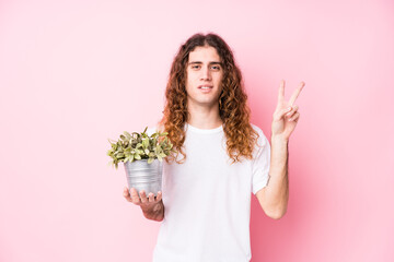 Long hair caucasian man holding a plant showing number two with fingers.