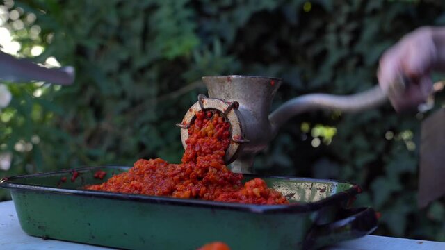 Close up outdoor on female hand on grinder mill for vegetables preparing paprika baked red pepper for ajvar national dish in balkan - healthy organic food concept