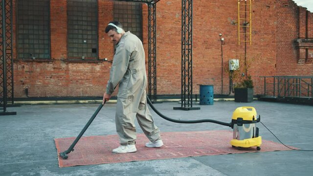 Talented janitor young handsome man stops vacuum cleaning and doing exciting break down moves on the rooftop. Urban environment. Skillful service worker. Fun.