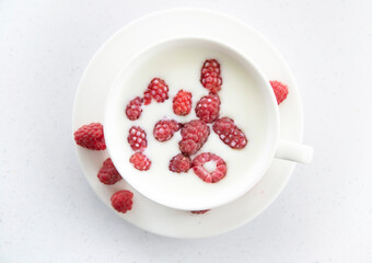 white mug with milk and raspberries in milk on a white background.