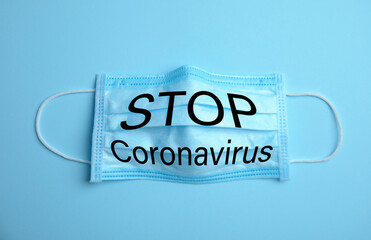 Medical mask with text Stop Coronavirus on light blue background. Protective measures during pandemic