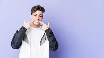 Young caucasian man isolated on purple background smiles, pointing fingers at mouth.