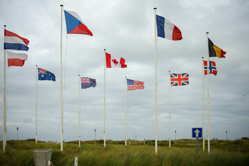 Flags of the countries that formed the Allies in World War 2, including Canada, France and America, under a cloudy grey sky. Image has copy space.