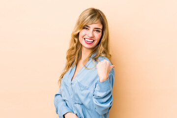 Young blonde caucasian woman points with thumb finger away, laughing and carefree.