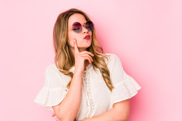 Young caucian woman with glasses isolated on pink background contemplating, planning a strategy, thinking about the way of a business.