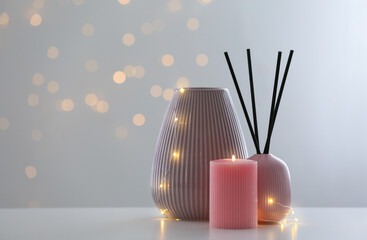 Vase, burning candle and reed diffuser on table against blurred background with bokeh effect. Space...
