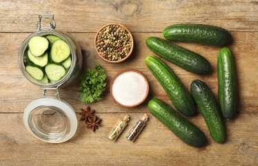 Pickling jar with fresh ripe cucumbers and spices on wooden table, flat lay