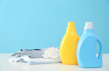 Detergents and children's clothes on white table near light blue wall. Space for text