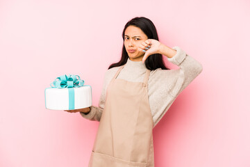 Young chinese woman holding a cake isolated showing a copy space on a palm and holding another hand on waist.