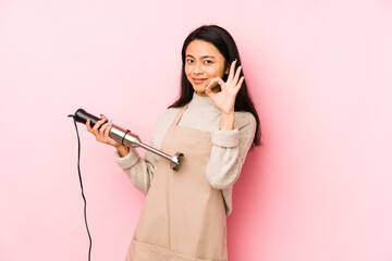 Young chinese woman holding a mixer isolated showing fist to camera, aggressive facial expression.