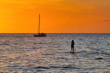 Silhouetted stand up paddle boarder with silhouetted boat at sunst on Maui.