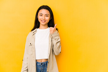 Young chinese woman isolated on a yellow background smiling and raising thumb up