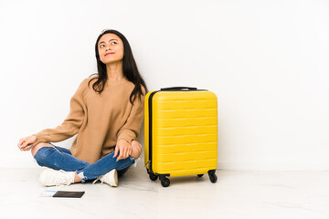 Young chinese traveler woman sittting on the floor with a suitcase isolated dreaming of achieving goals and purposes