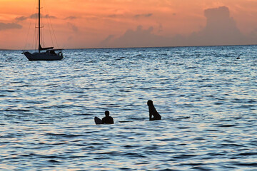 Two silhouetted surfers looking out towards incoming surf in Lahaina harbor on Maui.