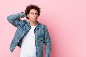 Fototapeta premium Curly mature man wearing a denim jacket against pink background touching back of head, thinking and making a choice.