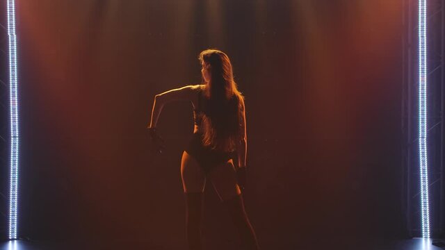 Passionate young brunette shot close up dancing captivatingly in black womanish lingerie in a dark studio with staged light. Silhouette of a slender toned body. Slow motion.