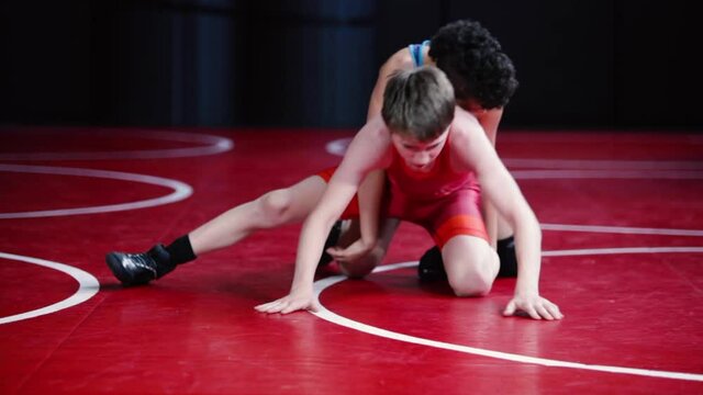 Youth wrestlers in red and blue singlets wrestling in the top and bottom position