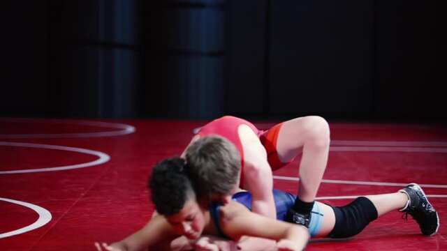 Youth wrestlers in red and blue singlets live wrestling in the top and bottom position