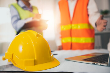 yellow helmet of construction worker on meeting table  in office with engineer planning background