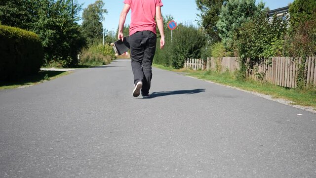 Young man or youth kicks up the tail of his skateboard, catches it and walks away with it in hand