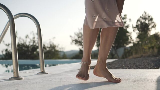 Young woman with long dress and straw hat dancing and spinning barefoot alongside a pool on a mountain in Ibiza, Spain at sunset. Shot in slow motion.