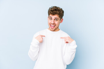 Young blond curly hair caucasian man isolated surprised pointing with finger, smiling broadly.