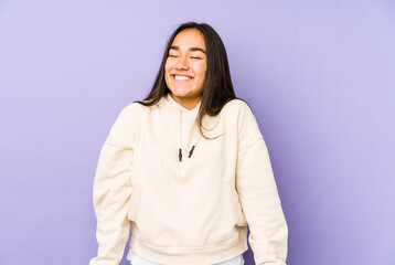 Young woman isolated on a purple background laughs and closes eyes, feels relaxed and happy.