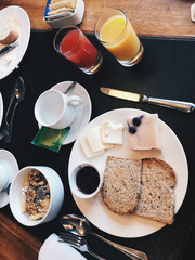 Healthy and vegetarian breakfast consisting of fruit salad with seeds and nuts, bread, green tea, cake, and squeezed orange and strawberry juice on a table with black leather