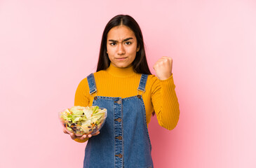 Young asian woman holding a salad isolated showing fist to camera, aggressive facial expression.