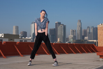 Fototapeta premium Tall young urban female enjoying the sunshine on a city rooftop overlooking Downtown Los Angeles.