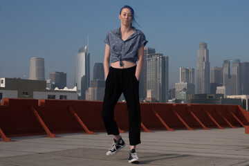 Tall young urban female enjoying the sunshine on a city rooftop overlooking Downtown Los Angeles.