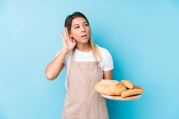 Young caucasian baker woman isolated trying to listening a gossip.
