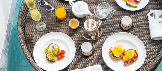 Floating Breakfast tray in swimming pool at luxury hotel or tropical resort villa, fruits; mango, watermelon dragon and passion fruit, food, bread, coffee, tea, wine and orange juice. Exotic summer
