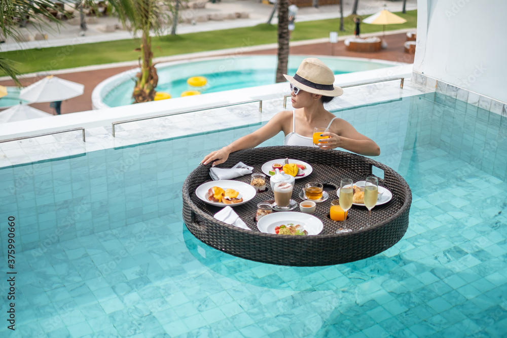 Wall mural Happy woman in white swimsuit having Floating Breakfast tray in luxury pool hotel, young female with sunglasses enjoy in tropical resort. Relaxing, Exotic summer travel, holiday, vacation and weekend