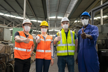 Teamwork of multiethnic engineer with workers giving thumbs up and wearing surgical mask to prevent covid-19 in manufacturing factory