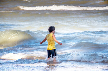 Young boy appears to be commanding wild waves, as he stands on a beach on the shores of Lake Michigan USA