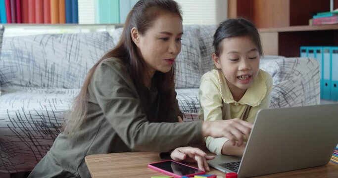 Young mother helping daughter do homework on laptop learning online