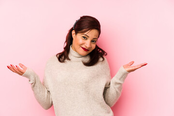 Middle age latin woman isolated on a pink background doubting and shrugging shoulders in...