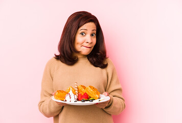 Middle age latin woman holding a waffle isolated confused, feels doubtful and unsure.