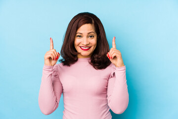 Middle age latin woman isolated indicates with both fore fingers up showing a blank space.