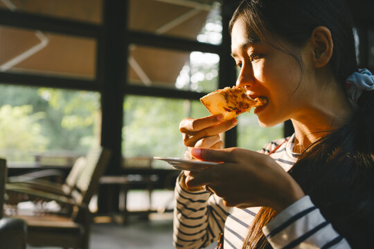 Happy young Asian woman eating pizza at restaurant, Crispy thin crust hawaiian pizza origin homemade.