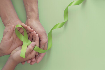 Adult and child hands holding Lime Green Ribbon on green background, children Mental health awareness and Lymphoma Awareness, world mental health day, world kidney day