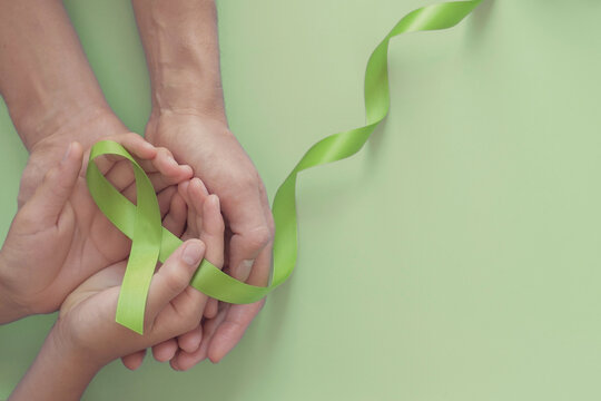 Adult And Child Hands Holding Lime Green Ribbon On Green Background, Children Mental Health Awareness And Lymphoma Awareness, World Mental Health Day, World Kidney Day