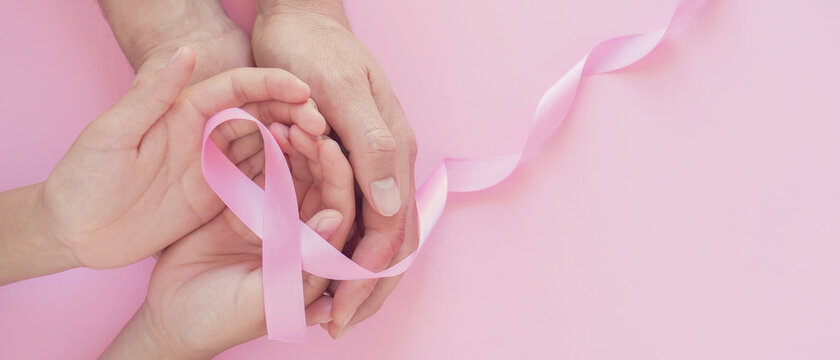 Adult and child hands holding pink ribbon, breast cancer awareness, October pink, World cancer day concept