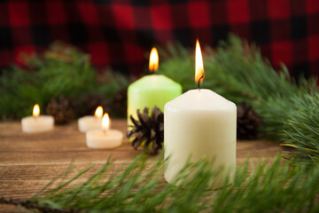Fototapeta na wymiar Christmas background, a composition of candles, a blanket, a fir tree, cones and a place for text on a wooden background, focus on the middle plan