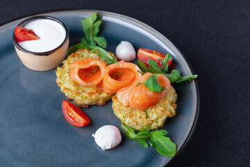 Portion of zucchini fried pancakes with salmon, cherry tomato