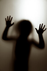 Ghost concept shadow of a child behind the matte glass blurry hand and body soft focus.